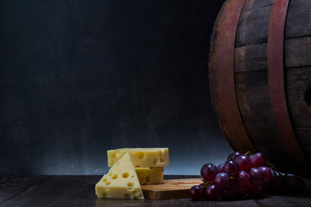 Cheese, grapes and wooden barrel on dark background. Copy spaceの写真素材