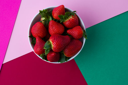 Strawberries in a bowl on a pink and green background.の写真素材