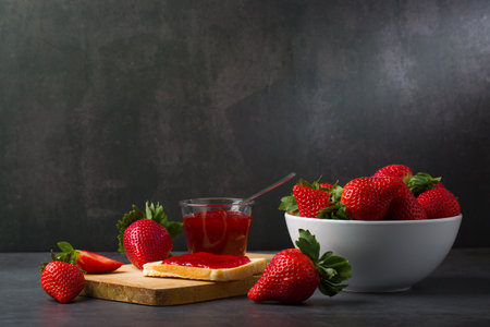 Strawberry jam in a bowl and fresh strawberries on a black backgroundの写真素材