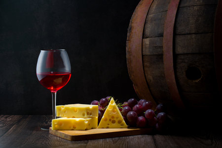 Glass of red wine, cheese, grapes and barrel on dark backgroundの写真素材