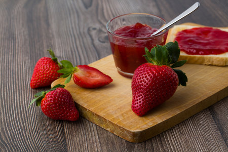 Strawberry jam and fresh strawberries on a cutting board on a wooden backgroundの写真素材