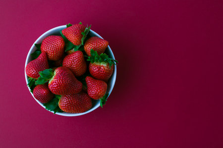 Fresh strawberries and green leaves in bowl isolated on red background, top viewの写真素材