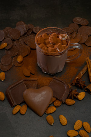 A cup filled with a hot chocolate drink sits surrounded by chocolate pieces, nuts, and spices on a...
