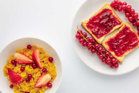A bowl of cereal is next to a plate with toast. The toast has jam spread on top and is garnished...