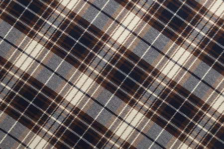Fabric with a plaid design in brown and navy blue is laid out on a table in a design studio. The...