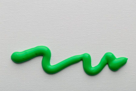 Bright green paint is arranged in a wavy line on a white canvas.