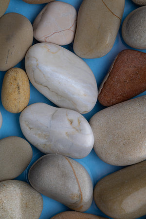 Stones of various sizes and colors are placed on a blue surface. The stones include smooth and rough...