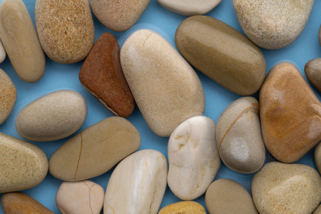 Different types of smooth stones are laid out on a blue surface. The stones show various colors and...