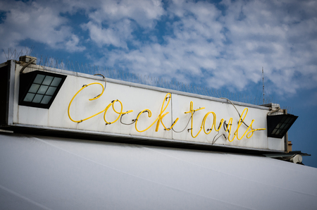 Illuminated sign with written cocktails with yellow colors on a blue sky and lots of clouds with lots of free space. Useful for advertising of restaurants and pubsの写真素材