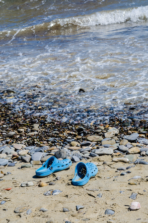 Blue beach shoes between the beach and the sea. Useful for indicating a hot summer seasonの写真素材