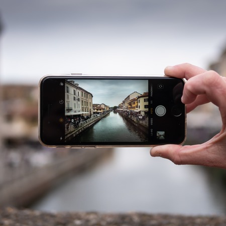 Milan, Italy - April 19, 2019: Tourist taking photo of Naviglio canal in Milan Italy with a mobile phone. Travel concept. Square viewのeditorial素材