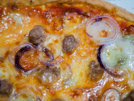 Close up of an Italian pizza with sausage, red onion, mozzarella and tomatoの写真素材