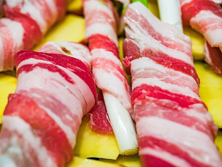 Raw spring onion with rolled bacon. Typical Sicilian street dish called 'Cipollata' roasted on the grill and roasted potatoes as a side dish. Horizontal view.の写真素材