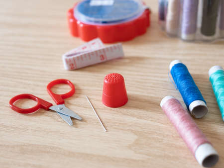 Spools of thread, bobbin, scissors and sewing accessories on a wooden background with shallow deep...