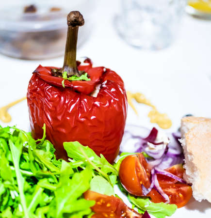 Baked stuffed red peppers with a side of green salad, cherry tomatoes and sliced red onion. Square...