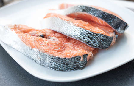 Close up of three fresh salmon slices, in a white plate, on a slate table. Tasty food from Italian cuisine and from the Mediterranean sea. Concept for a tasty and healthy meal. Horizontal view.の写真素材