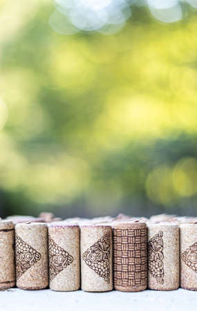 Vertical row of corks, on a white wooden table and with a natural green background. Green out of focus negative space. Concept of nature outdoors. Vertical viewの写真素材