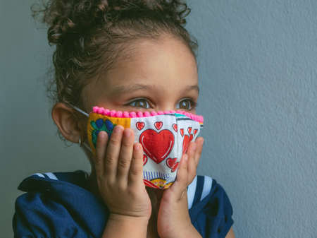 A little girl with a mask with hearts is clutching her face