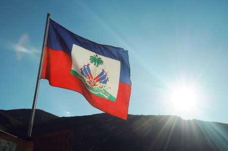 Haitian flag blowing in the breeze with the Haitian mountains behind and a sunset casting rays of lightの写真素材