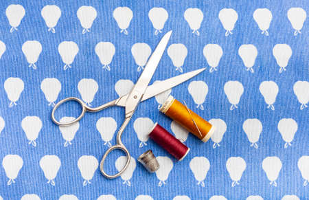 Scissors, a needle and two spools of red and yellow thread together with a thimble on a blue cloth.