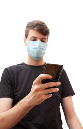 Young man wearing a face mask during the Coronavirus COVID-19 virus pandemic while checking his mobile phone.の写真素材
