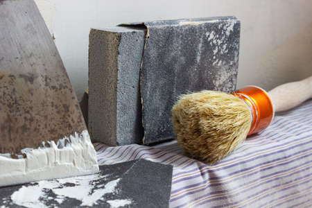 A putty knife, paint brush, sandpaper and wall sealing paste on a radiator ready to start renovating...