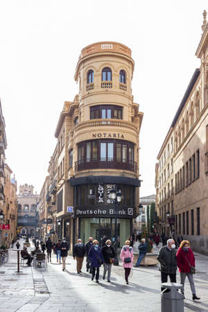Salamanca, Spain - January 19, 2021: People wearing a protective mask due to the covid-19 pandemic walking through the streets of Concejo and Zamora next to the Deutsche Bank tower buildingのeditorial素材