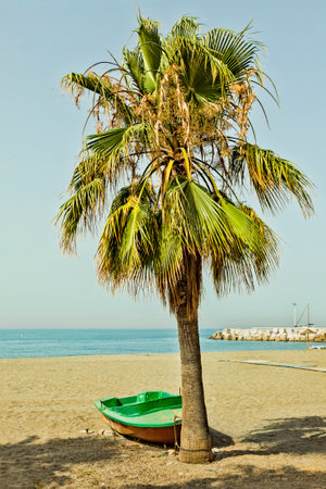 A small wooden boat used by fishermen beached on the sandy beach next to the Mediterranean Seaの写真素材