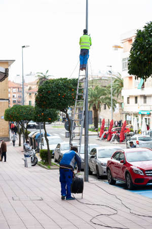 Plasencia, Spain - February 17, 2021: An operators of the communications company C Plaza Electricity worked in street lighting maintenance, up a high staircase with a lamppost.のeditorial素材