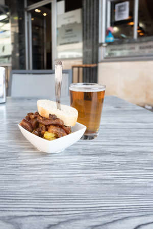 Close-up photo of a fresh beer in a glass and an aperitif of a serving of pork cheeks on the terrace of a Spanish bar. (spanish morros)の写真素材