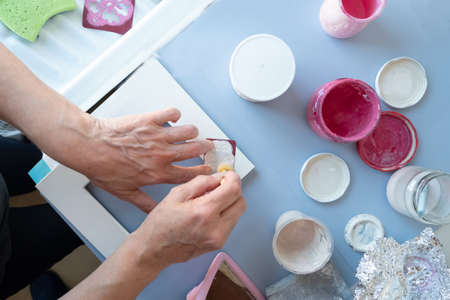 Mature woman with is doing crafts in the laundry room of your house. She is decorating a white watering can with pink flowers with a wooden brush using a pink flower design template or stencilの写真素材