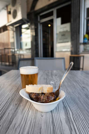 Close-up photo of a fresh beer in a glass and an aperitif of pork cheeks on the terrace of a Spanish bar. Pub.の写真素材