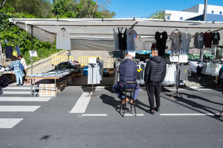 Plasencia, Spain - March 23, 2021: A vendor sitting on a stool next to his stall in a clothing and accessories street market held every Tuesday in Plasenciaのeditorial素材