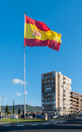 Plasencia, Spain - March 18, 2021: A huge flag of Spain flutters its colors in the wind in a roundaboutのeditorial素材