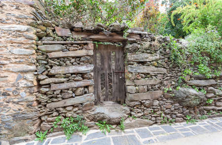 Robledillo de Gata, Spain - March 27, 2021: Entrance to a vegetable garden with an old wooden door with a rusty iron bolt in a slate wallの写真素材