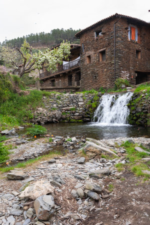 Robledillo de Gata, Spain - March 27, 2021: A waterfall of crystalline and cold water in the Arrago river channel with a typical background houses built with slate and adobe.のeditorial素材