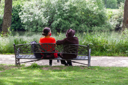 Plasencia, Spain - March 24, 2021: An elderly mother and her daughter sit on a bench in a public park while chatting and watching the wild animals.のeditorial素材