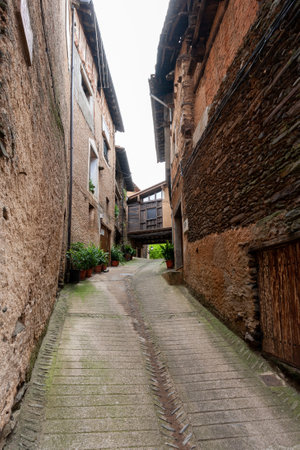 Robledillo de Gata, Spain - March 27, 2021: A narrow street of old houses built with adobe, slates and wood and in the background an elevated walkway made of wood joins two housesのeditorial素材