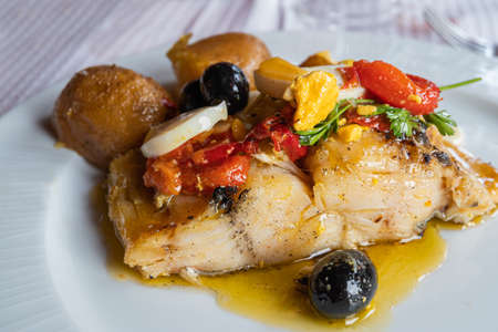 Closeup of a plate of good cod from the Atlantic sea with potatoes, onion, egg, red pepper, olives...