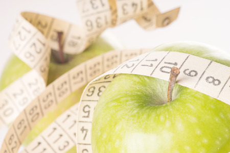 two green apples with measuring tape over a white backgroundの写真素材