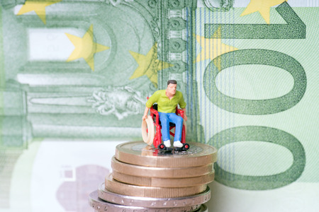 Wheelchair user on a stack of euro coins with euro banknoteの写真素材