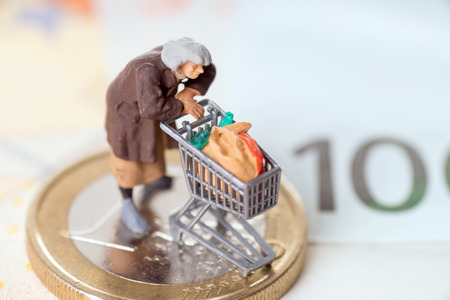 Old woman with shopping cart on a euro coin with banknotesの写真素材