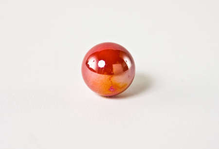 A red and orange glass marble set against a white background.  The marbles colors blend in a...