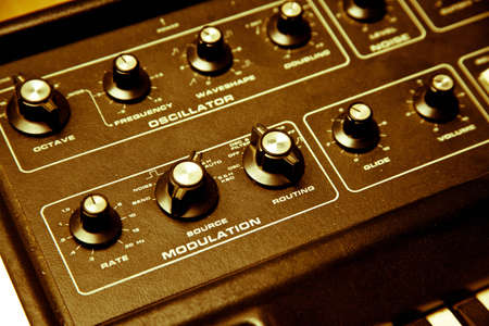 A yellow hued shot of a synthesizer and its knobs and keys.  the synthesizer is on top of a wood table.  detail is on the modulation and oscillator.の写真素材