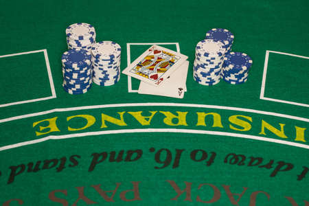 Several stacks of blue and white poker chips are arranged on either side of two playing cards on a green card table  There is upside-down lettering on the card table のeditorial素材
