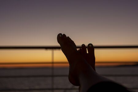 silhouette of feet relaxing on a ships rail