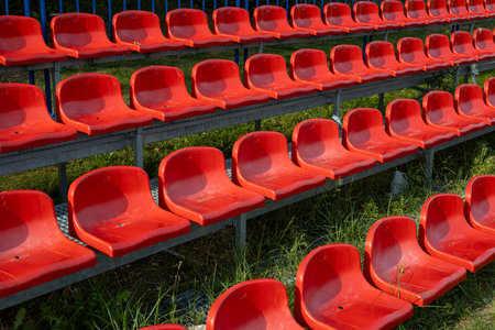 Red plastic seats on the tribune of a football stadium in summerの写真素材