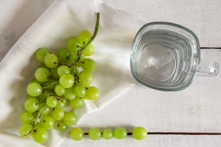 green grapes in still life with a glass of water and white background