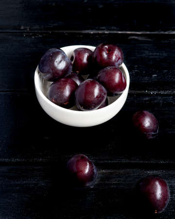 prunes passed in a white bowl that are on a black wooden board in the shape of a still life