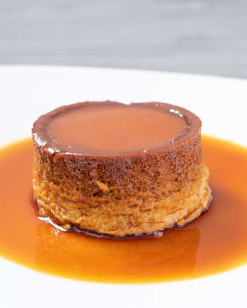 small mexican neapolitan custard with caramel all around on a white plate with an unfocused gray wooden backgroundの写真素材